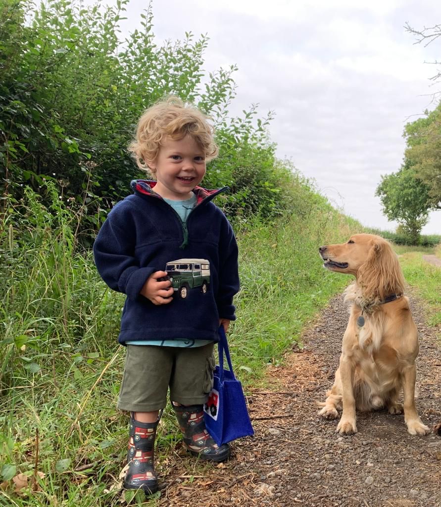 Child standing on a path with a land rover fleece dog, holding a toy car